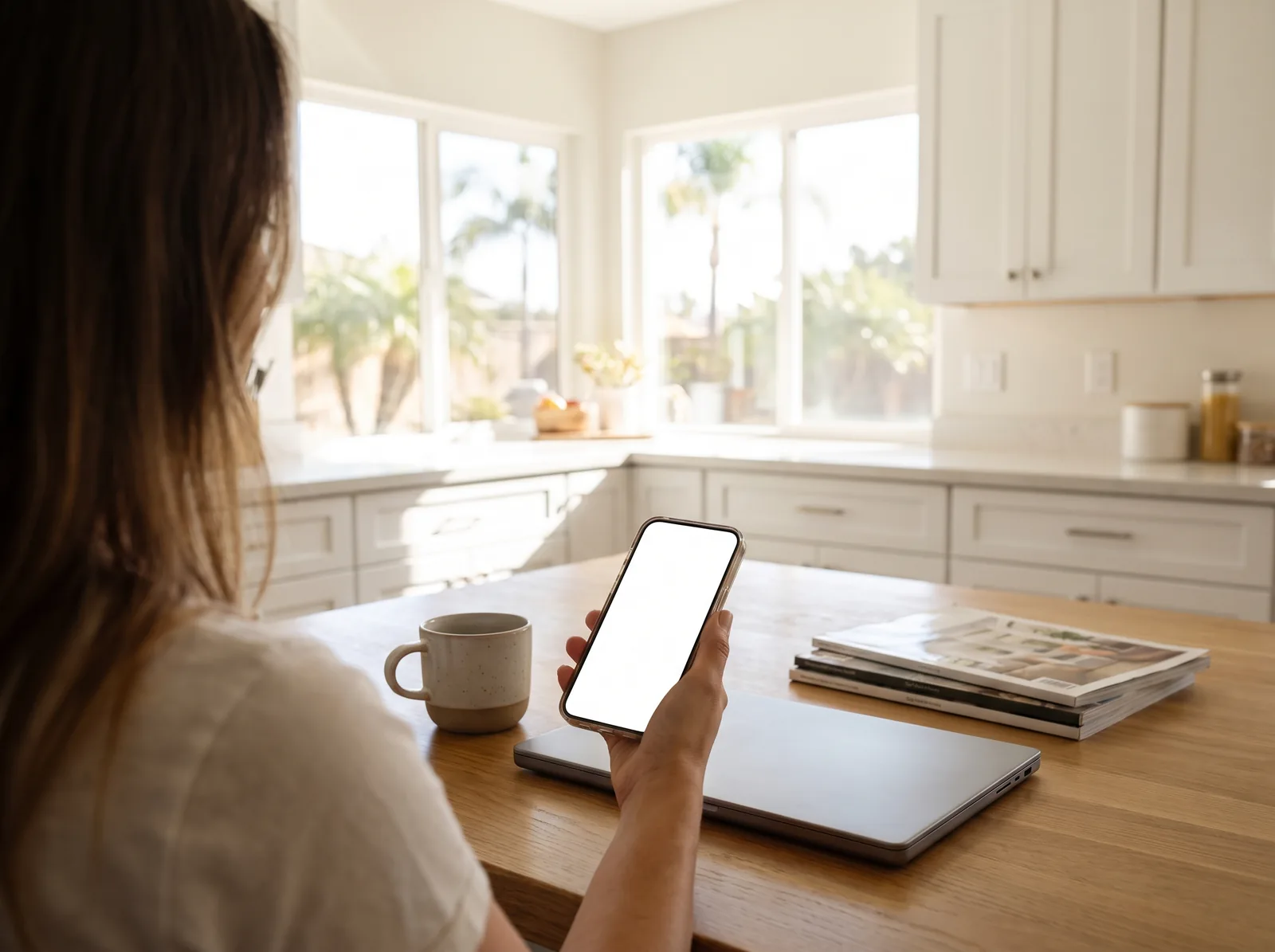 A woman at a sunny kitchen table holding her phone